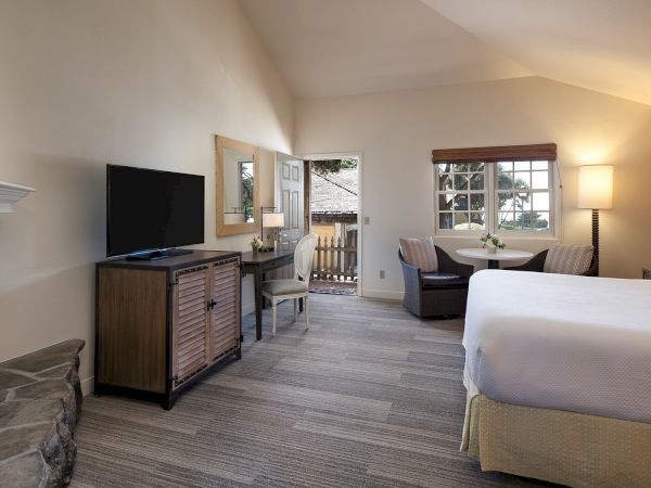 Cozy hotel suite with two queen beds, a sitting area, desk, fireplace, flat-screen TV, and a small deck framed by a bright, inviting interior, ending with a period.