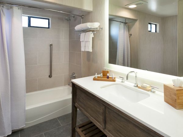 A modern bathroom with a double-sink vanity, a bathtub with a shower curtain, light gray tiles, a wall mirror, and towel storage.
