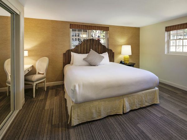 A cozy hotel room with a large bed, two nightstands, lamps, a sitting area, and windows letting in natural light.