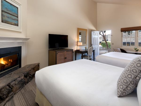 A hotel room with two queen beds, a fireplace, a flat-screen TV on a dresser, a desk and chair, and a balcony view through a doorway.