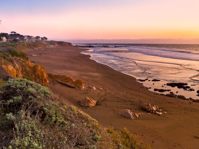 A serene beach scene at sunset with a cliffside and buildings in the distance.