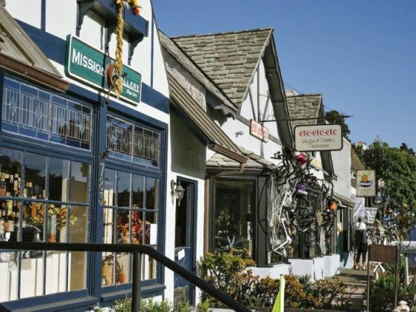 A sunny sidewalk lined with quaint shops and signs like Mission Gallery and etetec-etc, as people stroll by.