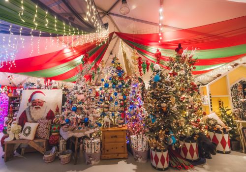 A festive Christmas shop with garlands, twinkling string lights, colorful draped fabric, and a decorated tree full of ornaments.