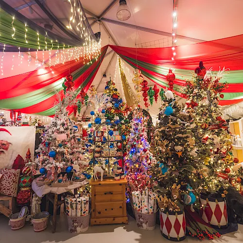 A festive Christmas shop with garlands, twinkling string lights, colorful draped fabric, and a decorated tree full of ornaments.