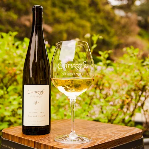 A Ctruzzola Vineyards bottle and filled wine glass rest on a wooden barrel in a lush vineyard garden. Cheers!